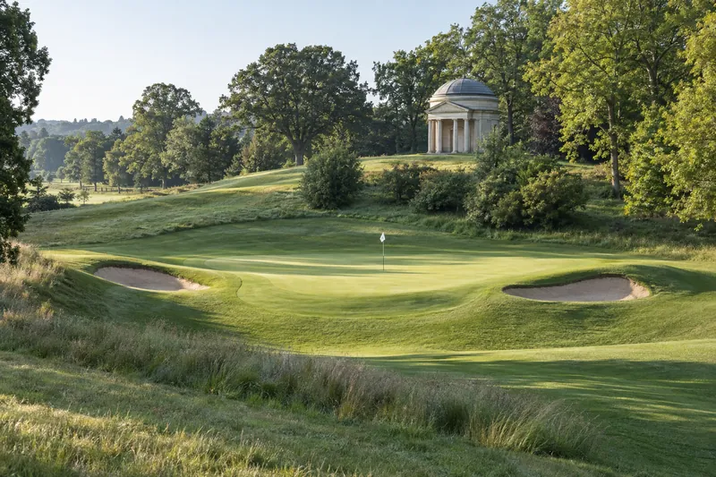The seventeenth green across a grassy hollow, two bunkers cut into its banks and the domed stone temple folly on the rise behind